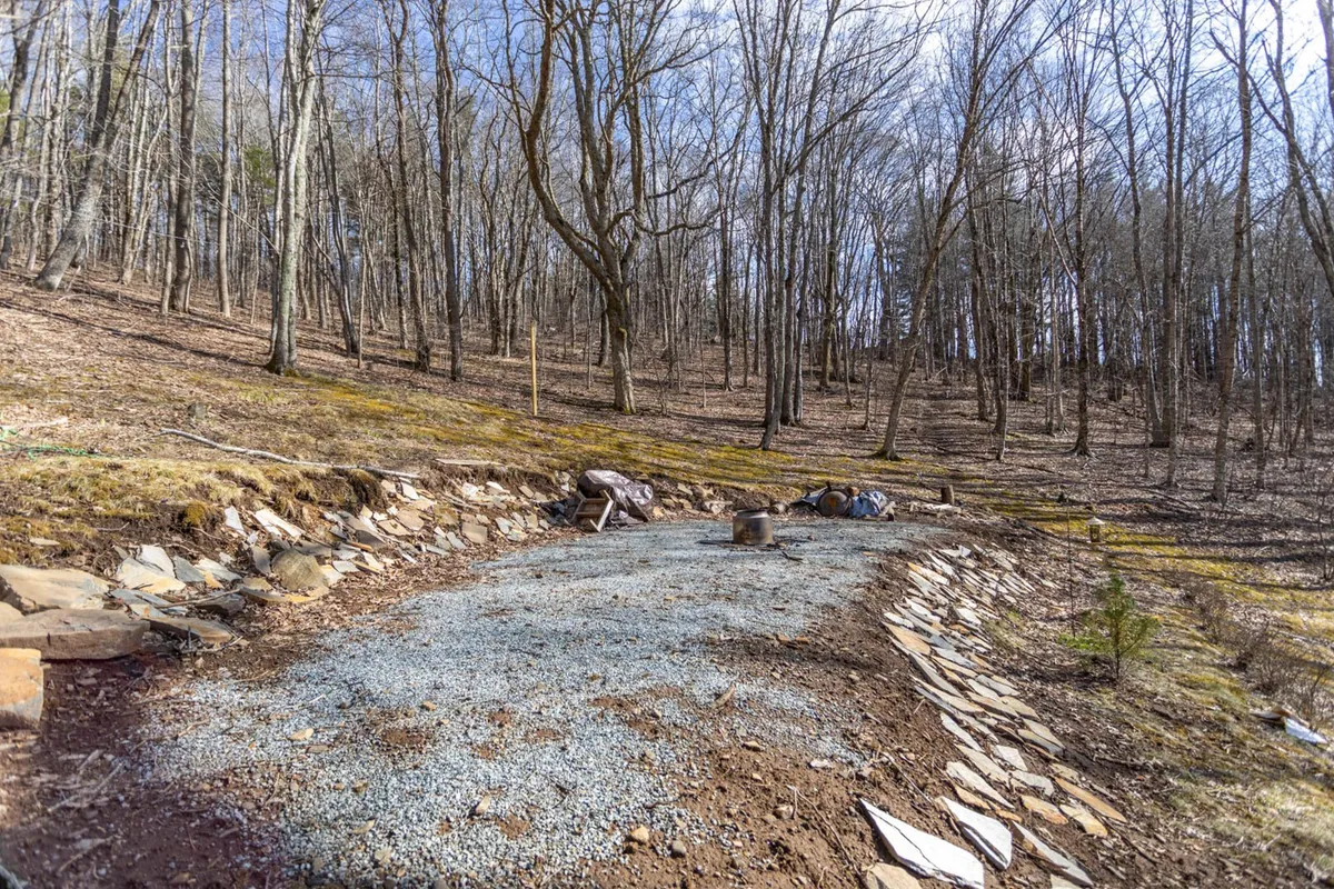 A peaceful gravel path winding through trees and stone elements immerses viewers in the natural environment surrounding the chalet. The tranquil mood evokes possibilities for hiking, nature walks, and observing local wildlife just steps from the property.