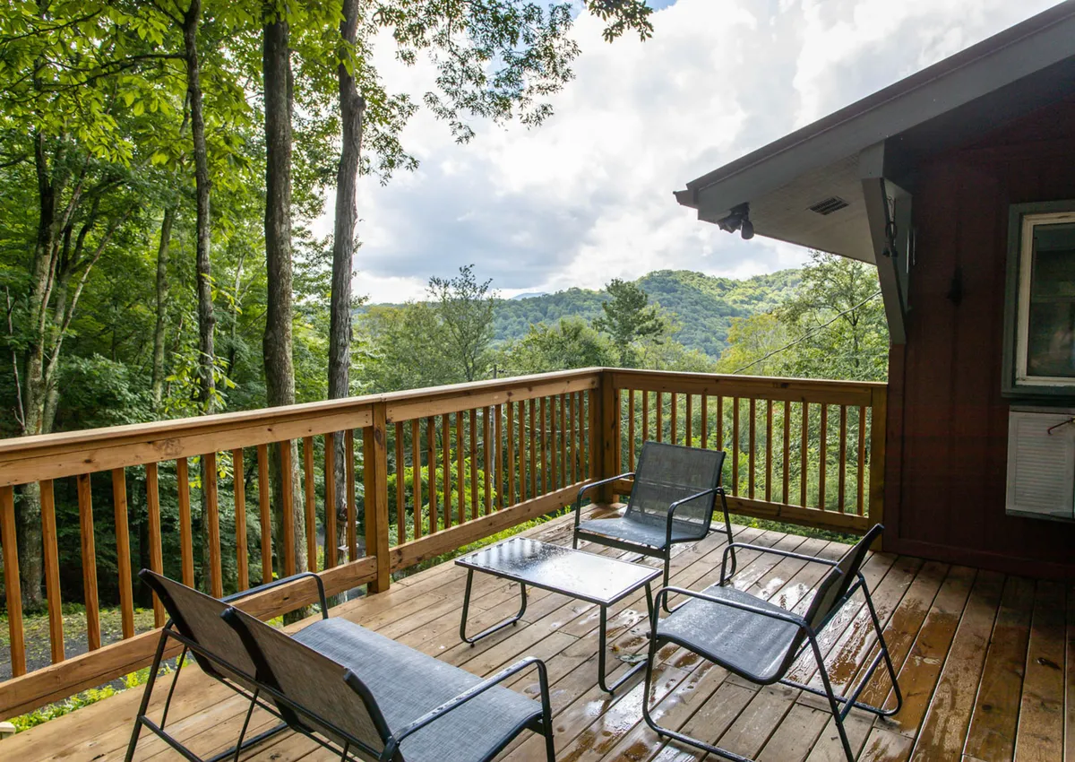 A tranquil scene showcasing a spacious wooden deck furnished with comfortable outdoor seating, opening up to sweeping mountain views. The deck is positioned at elevation, offering an unobstructed perspective of the surrounding hills and sky, perfect for enjoying both sunrises and sunsets. The setting is ideal for relaxing, socializing, or simply admiring nature.