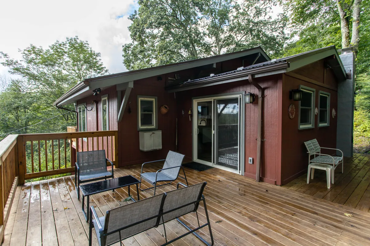 A charming deck area with wooden railings and inviting outdoor seating, set against a backdrop of tranquil greenery and distant hills. The scene suggests peaceful mornings or evenings spent outside, with space for families or friends to relax together and take in the scenery.