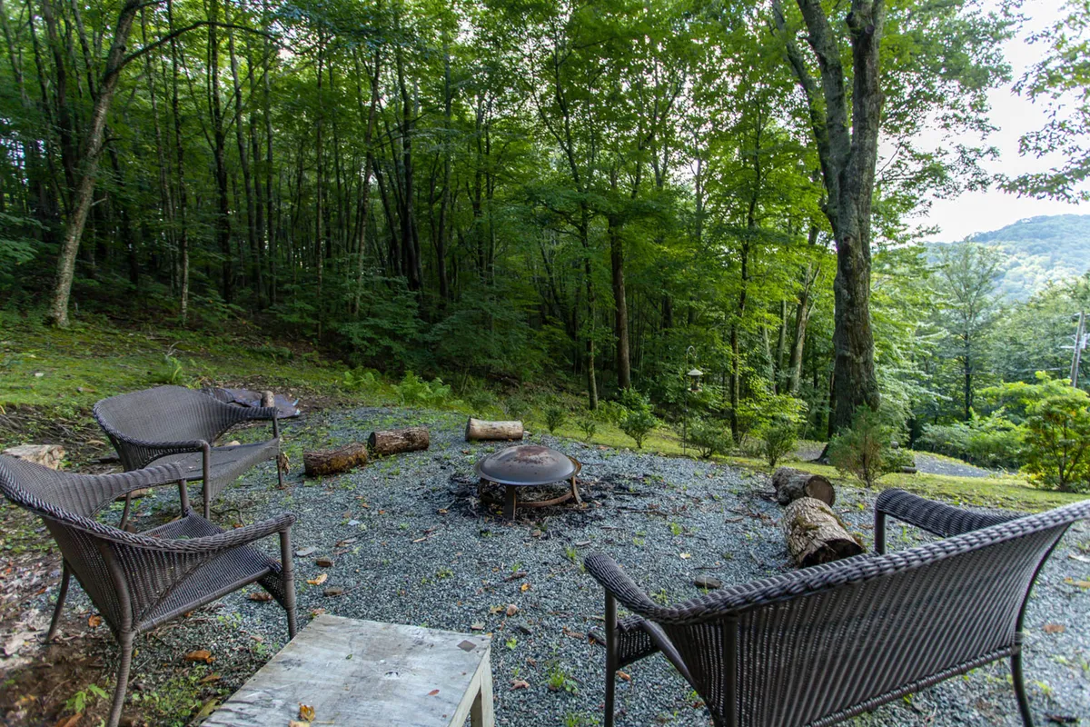 An inviting outdoor fire pit area surrounded by wicker chairs and nestled among trees creates a cozy communal space under the open sky. The setting suggests opportunities for evening storytelling, stargazing, and toasting marshmallows after a day of exploration.