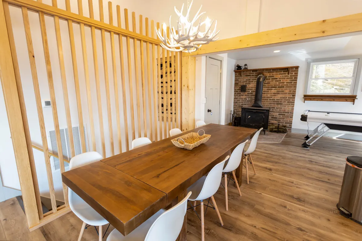 A large wooden dining table that comfortably seats eight is the centerpiece of this cozy dining area. An antler chandelier adds rustic charm, while a brick fireplace and wood accents create an atmosphere perfect for celebratory dinners and memorable gatherings.