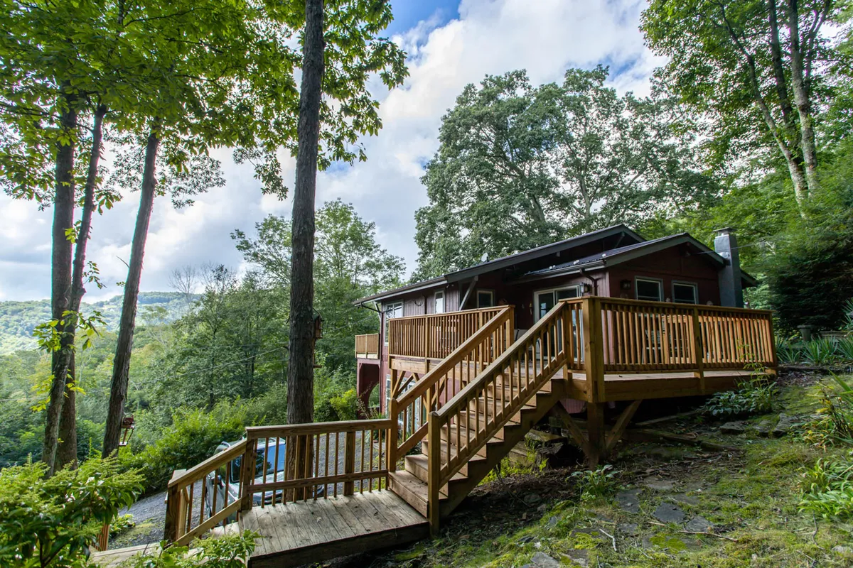 The image shows a spacious wooden deck surrounded by lush trees and the exterior of the home. The setting is serene and inviting, ideal for relaxing outdoors, watching sunsets, or preparing for a day’s exploration.
