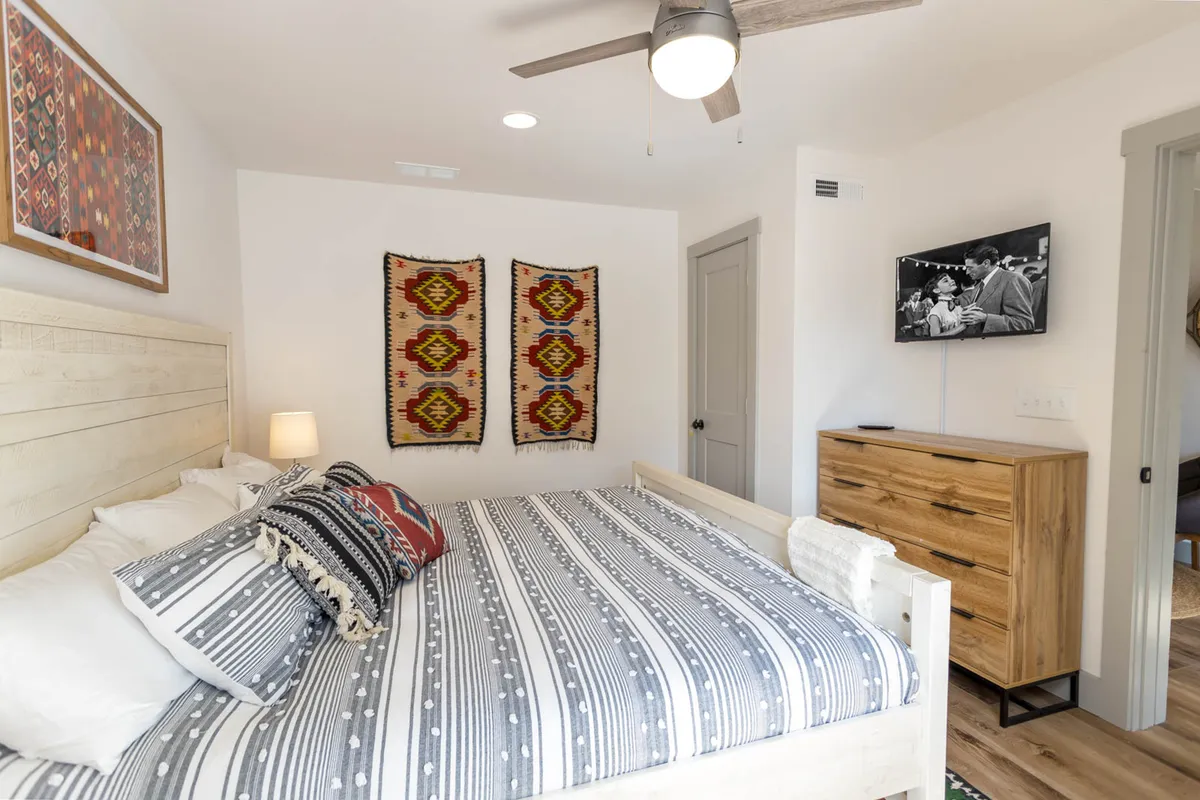 A restful bedroom highlighted by a plush King bed adorned with decorative pillows and cozy linens, woven wall hangings, a wooden dresser, and a television. The atmosphere is calm, offering an inviting retreat for recharging after mountain adventures.