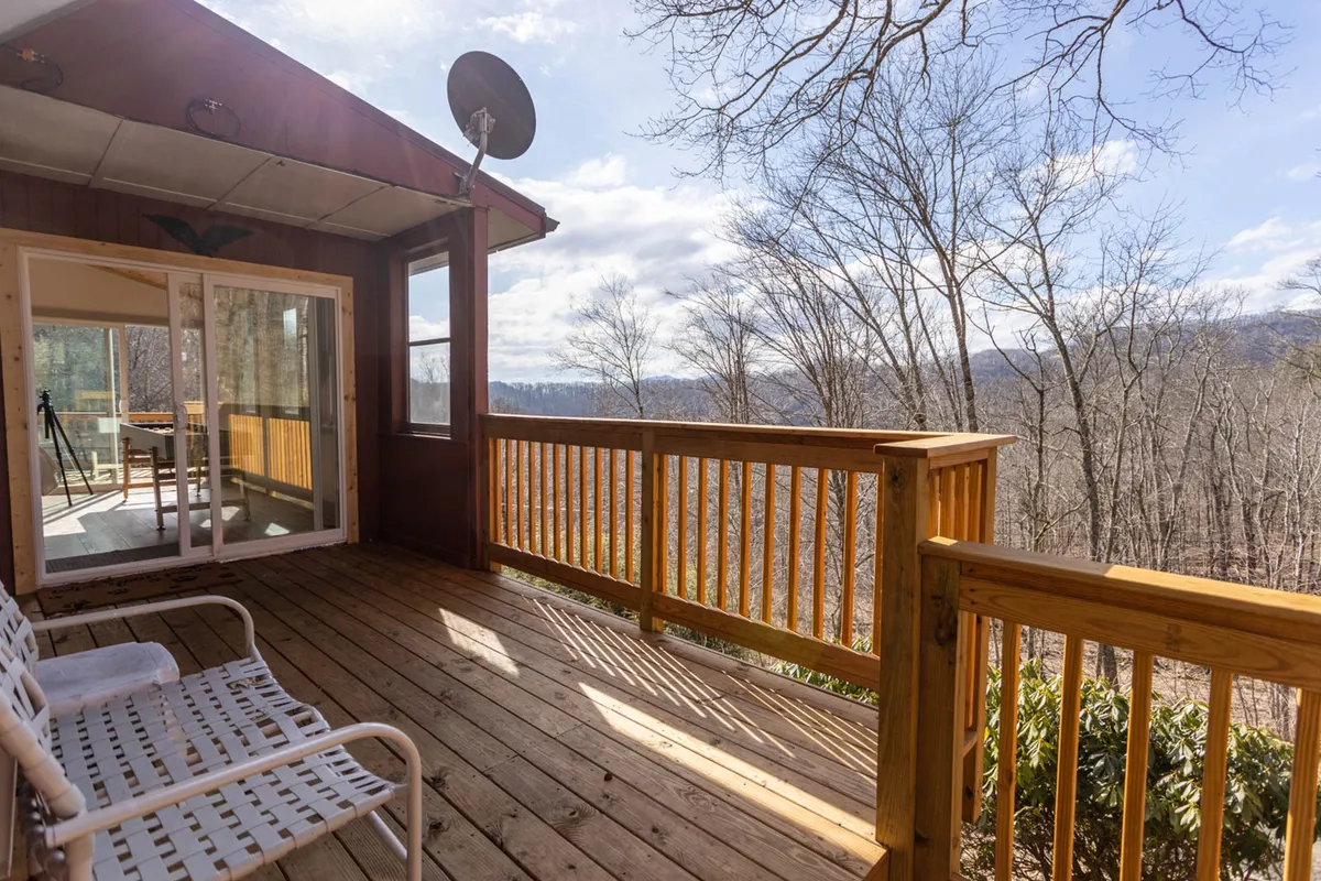 This image captures a wooden deck with a comfortable seating area, overlooking breathtaking mountain views. The setting is relaxed and open, with clear skies and natural surroundings visible, evoking the sense of elevation and connection to the outdoors that define this property.